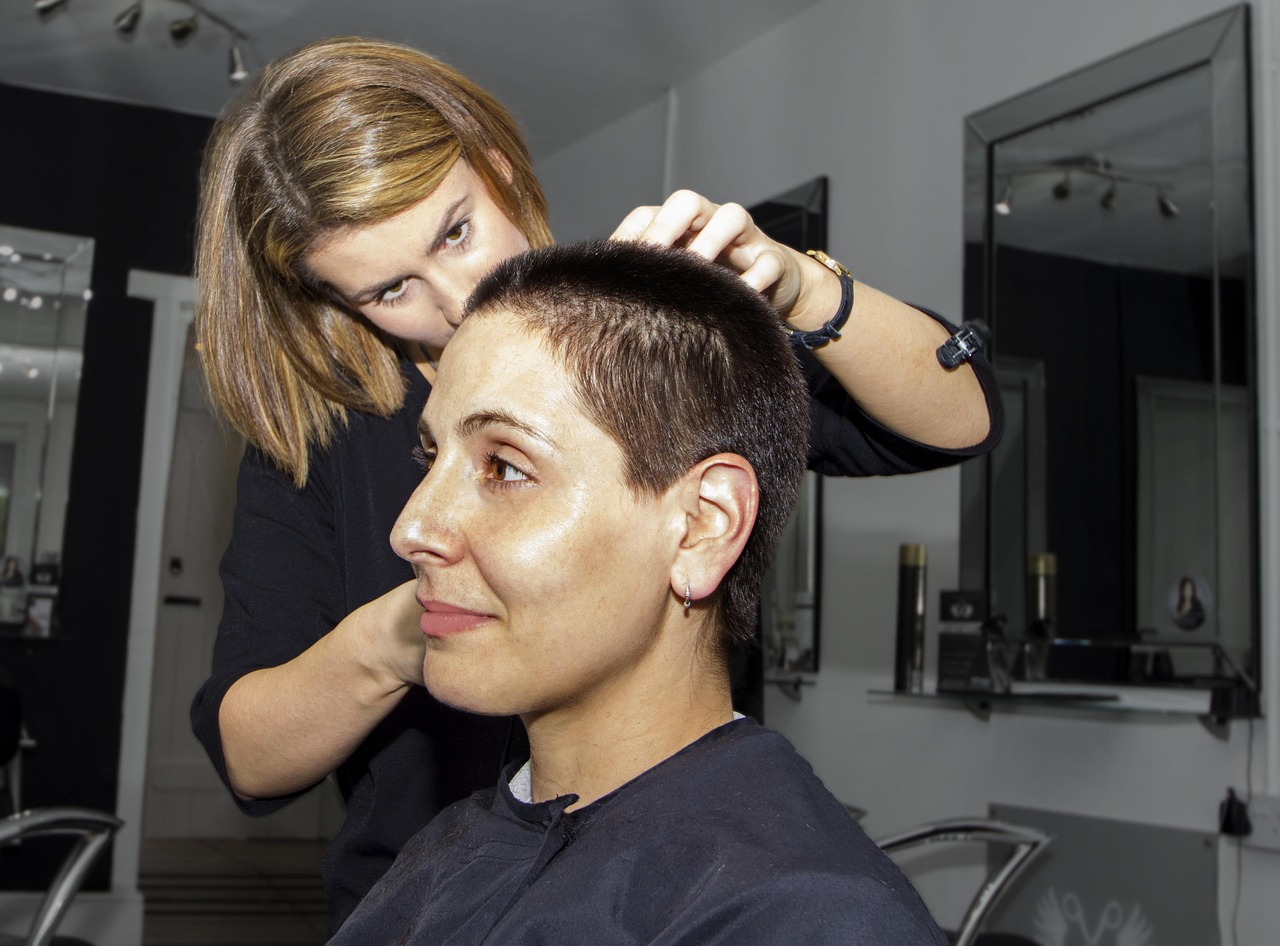 A woman stylist with a shoulder-length bob checking the top of a smiling client's short cropped haircut
